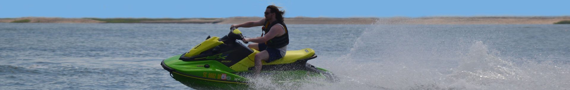 A man riding a blue and yellow jet ski against a sea and beach background.