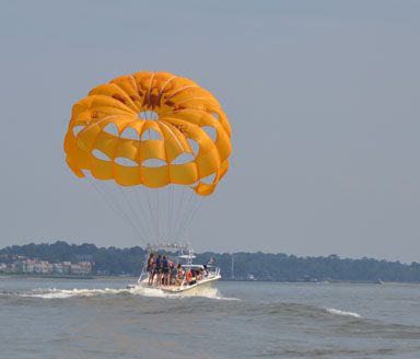 A yellow parasail wing attached to a motor with people sailing on it.