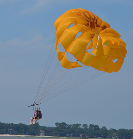 A full shot of a yellow parasail wing with three people hanging from it.